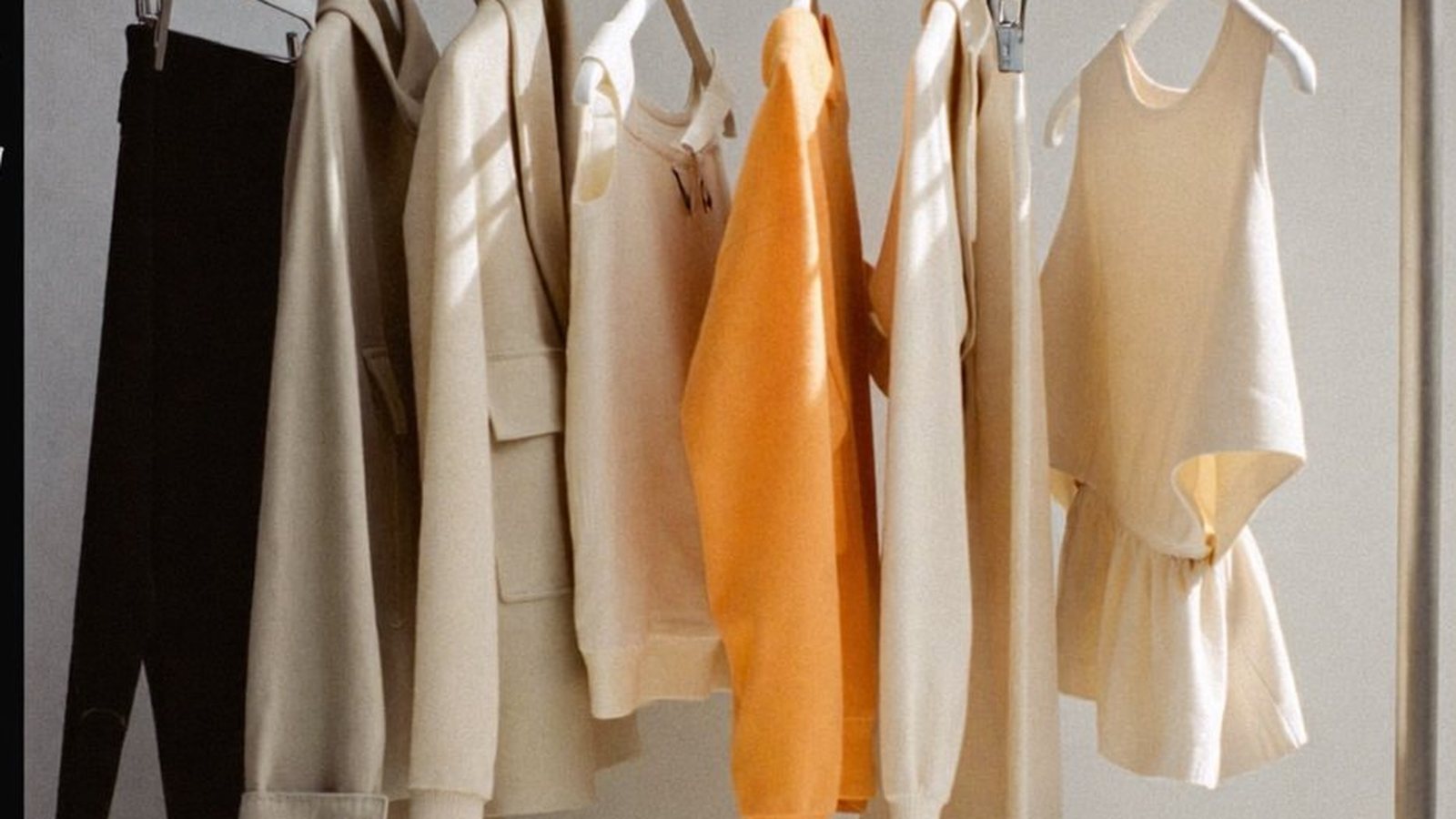 A garment rail, portfolio book and backpack against a plain wall